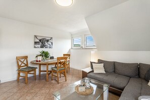 Een woonkamer met een bank, een eettafel met stoelen, een schilderij aan de muur en een raam met uitzicht.