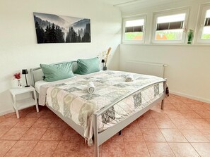 Un dormitorio con una cama, una mesita de noche, una ventana con persianas y un cuadro en la pared.