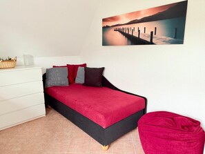 Un dormitorio con una cama, un tocador, una silla y un cuadro de una puesta de sol sobre el agua.