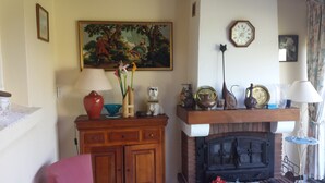 A living room with a fireplace, a painting, a clock, and various decorative items on shelves.