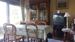 A dining area with a table, chairs, a cabinet with glass doors, a television, and a lamp.