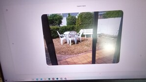A computer monitor displaying a view of an outdoor area with a white table and chairs, a bench, and a brick pathway.