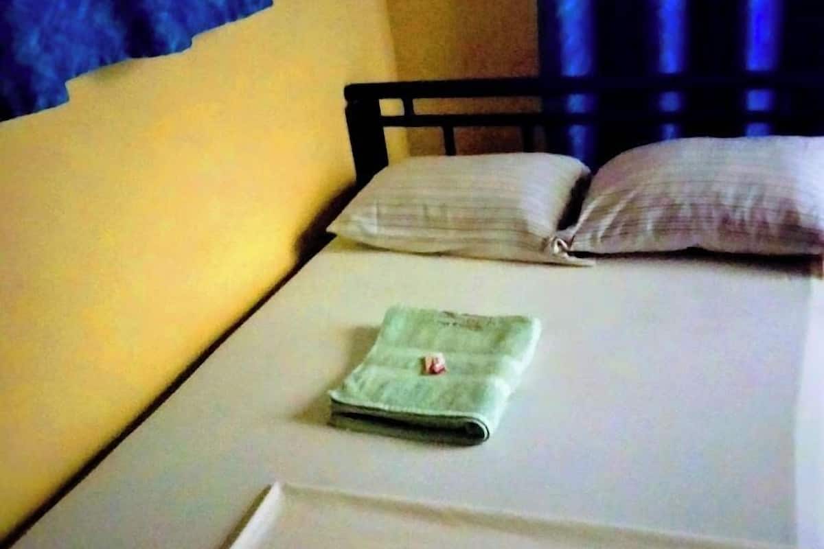 A single bed with a neatly folded green towel and a white pillow, a wooden headboard, and a blue curtain partially visible.