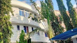 Un edificio a più piani con facciata curva, circondato da una vegetazione lussureggiante e un cortile lastricato.