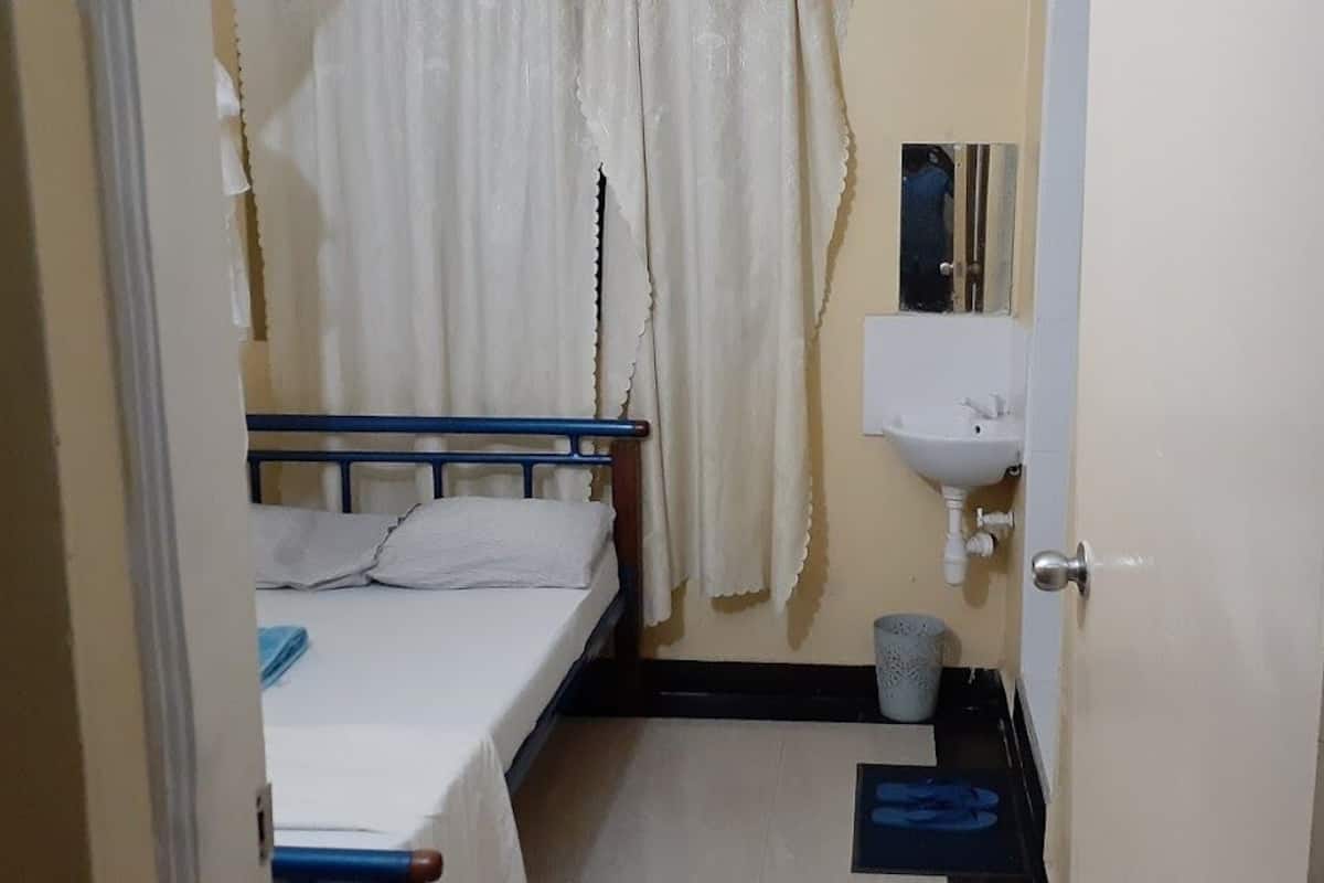 A small room with a bed, a bedside table, a sink, and a mirror.