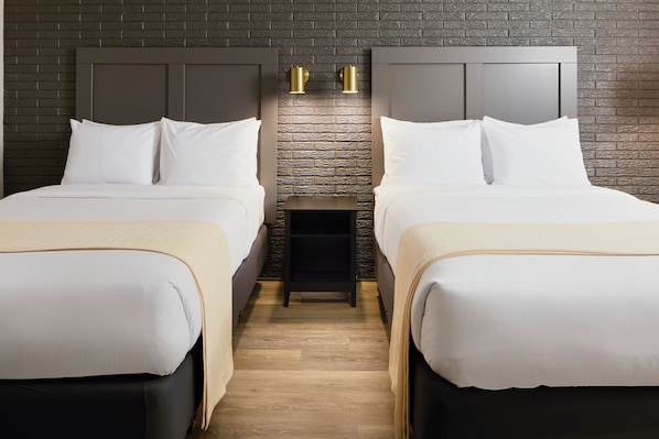 A hotel room with two beds, a brick-patterned headboard, and a small nightstand with two wall-mounted lights. - Hotel Arlington (Arlington)