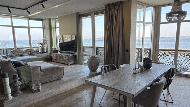 Amplia sala de estar con un gran ventanal con vista al mar, una mesa de comedor y una zona de estar acogedora.