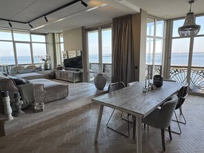 Un vaste espace de vie doté d’une grande fenêtre donnant sur la mer, d’une table à manger et d’un coin salon confortable.