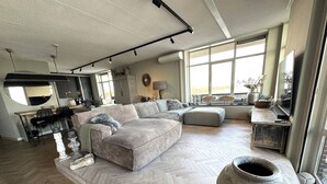 Un amplio espacio habitable con un sofá modular grande, piso con patrón de espiga y un jarrón de piedra considerable.