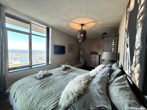 Een slaapkamer met een groot bed, een plafondventilator, een raam met uitzicht op het water en een dressoir.