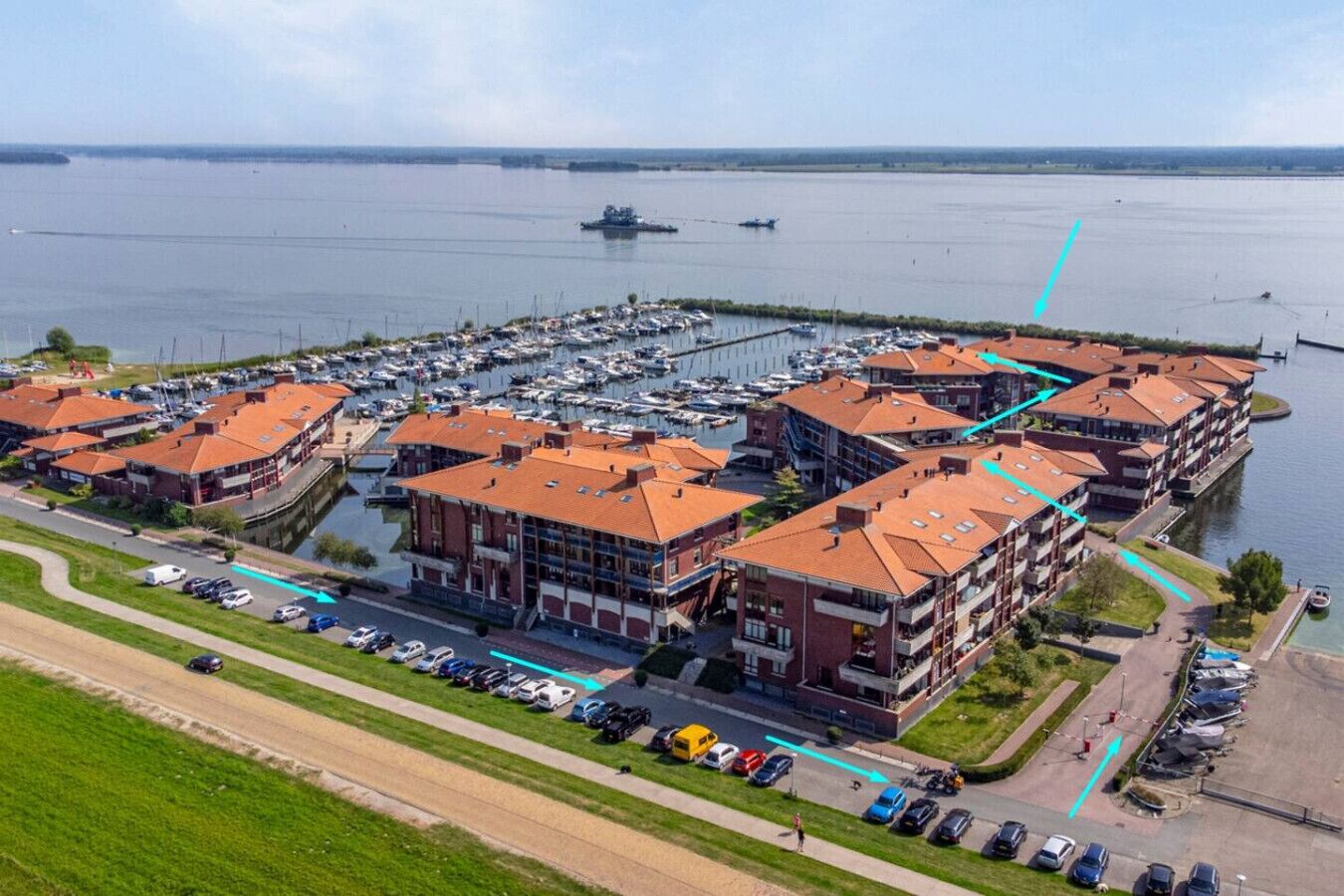 Un port de plaisance avec des bateaux, un parking et un bâtiment aux toits rouges.