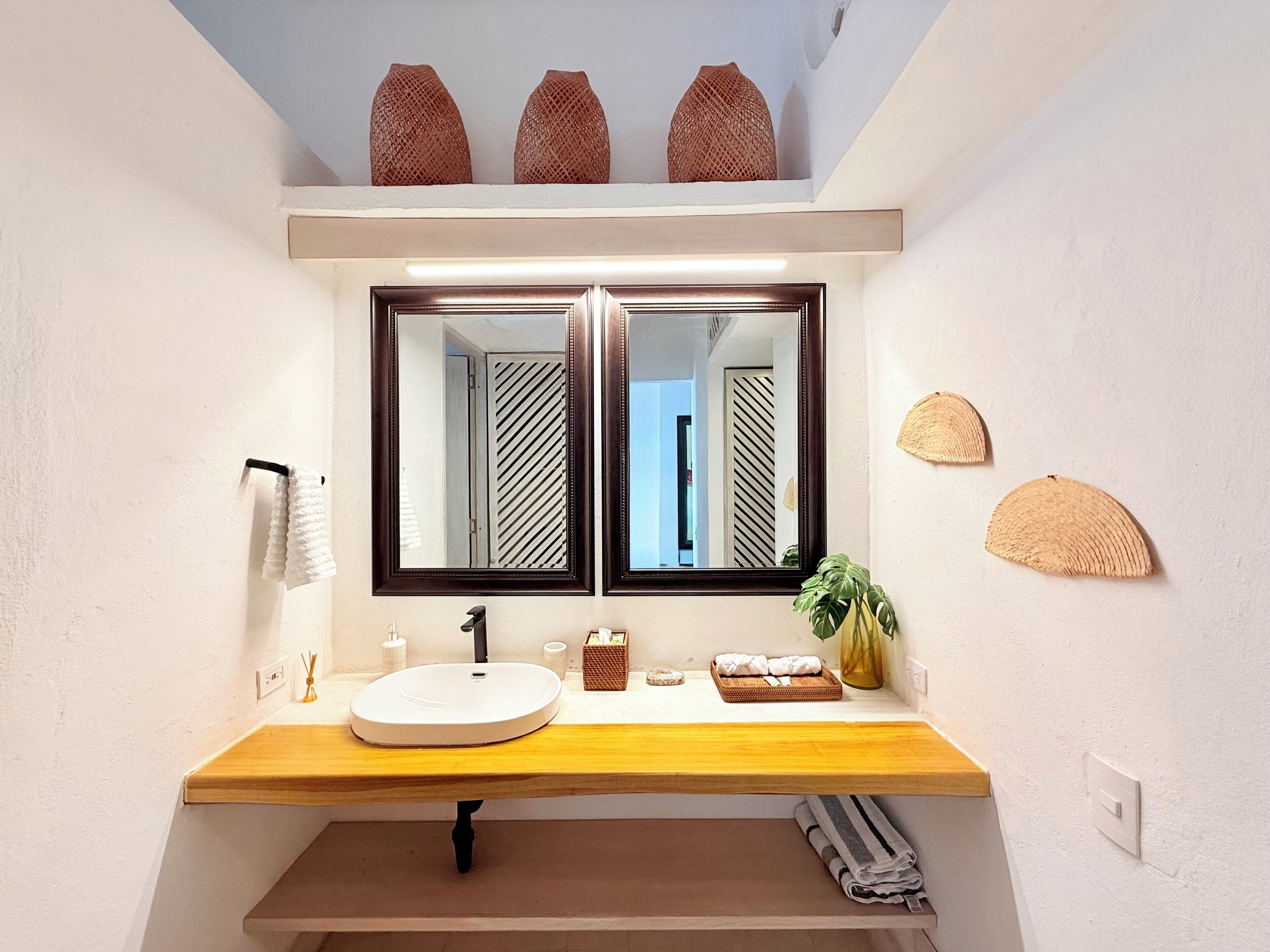 A bathroom with a wooden vanity, a round sink, two mirrors, and decorative vases on the wall.