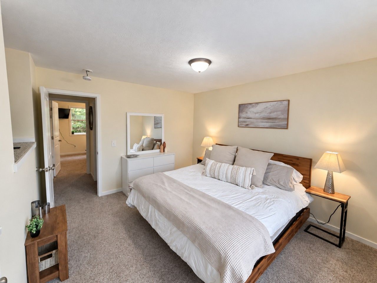 A bedroom with a bed, bedside tables, a dresser, a mirror, and a painting on the wall.