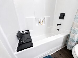 A white bathtub with a shower curtain, a black control panel, and a small shelf with toiletries.
