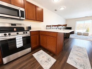 A modern kitchen with wooden cabinets, a stainless steel oven, a microwave, and a dining area with chairs.
