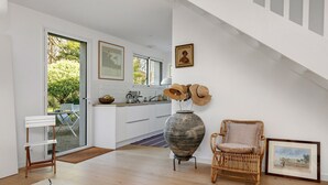 Una cocina moderna con armarios blancos, un jarrón grande, una silla de mimbre y un cuadro en la pared.