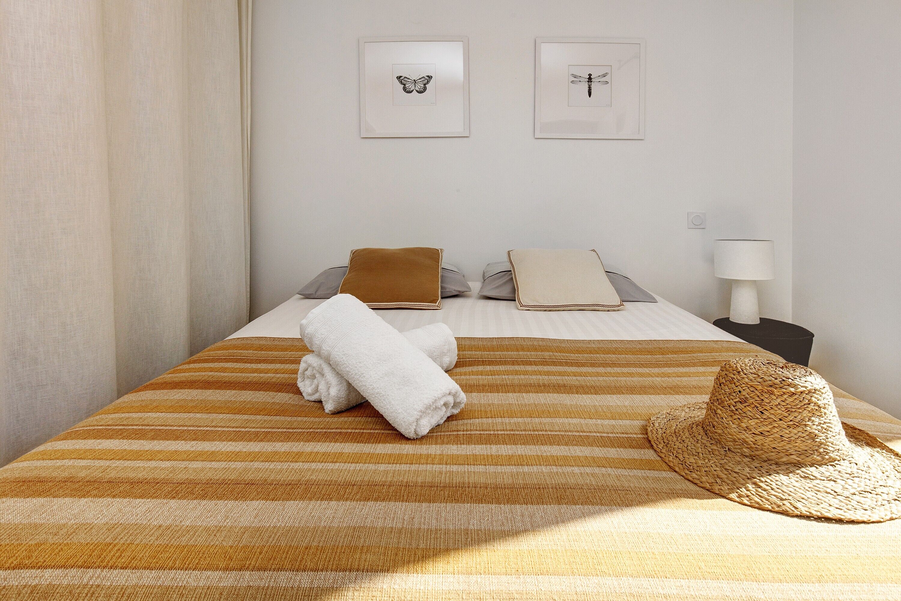 Una cama con ropa de cama a rayas, un sombrero de paja y dos cuadros en la pared.
