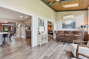 A spacious living area with a wooden floor, a dining area with bar stools, and a kitchen visible in the background. - Spacious Colorado Retreat, Game Room, Solarium, Patios & Mountain View’s (Evergreen)