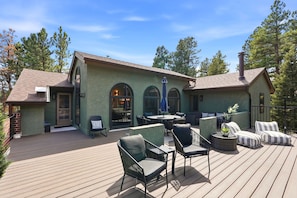 A deck with outdoor furniture, a building with arched windows, and a clear sky. - Spacious Colorado Retreat, Game Room, Solarium, Patios & Mountain View’s (Evergreen)