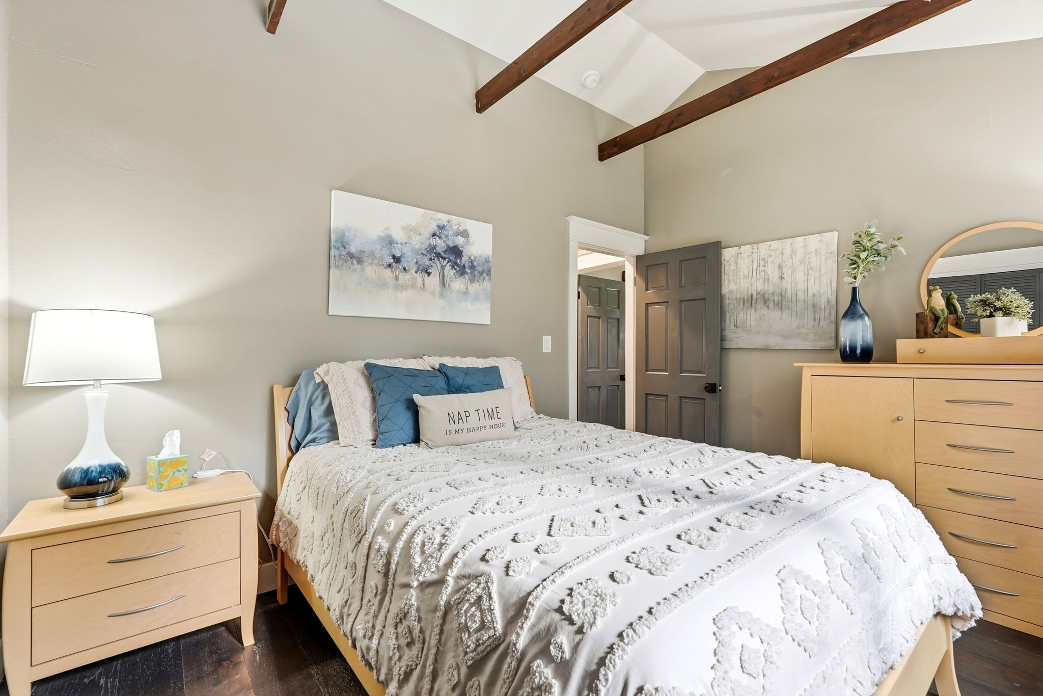 A bedroom with a bed, bedside tables, a lamp, and artwork on the walls.