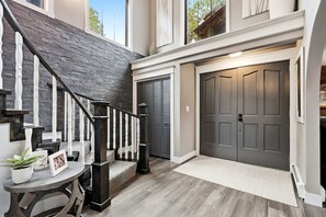 A modern interior with a staircase, a garage door, and a small table with a plant and picture frame. - Spacious Colorado Retreat, Game Room, Solarium, Patios & Mountain View’s (Evergreen)