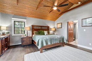 A bedroom with a wooden ceiling, a bed with a green quilt, a nightstand, a dresser, and a window with a view of trees. - Spacious Colorado Retreat, Game Room, Solarium, Patios & Mountain View’s (Evergreen)