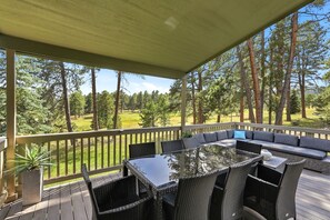 A covered outdoor seating area with a glass-top table and chairs, overlooking a grassy landscape with trees. - Spacious Colorado Retreat, Game Room, Solarium, Patios & Mountain View’s (Evergreen)