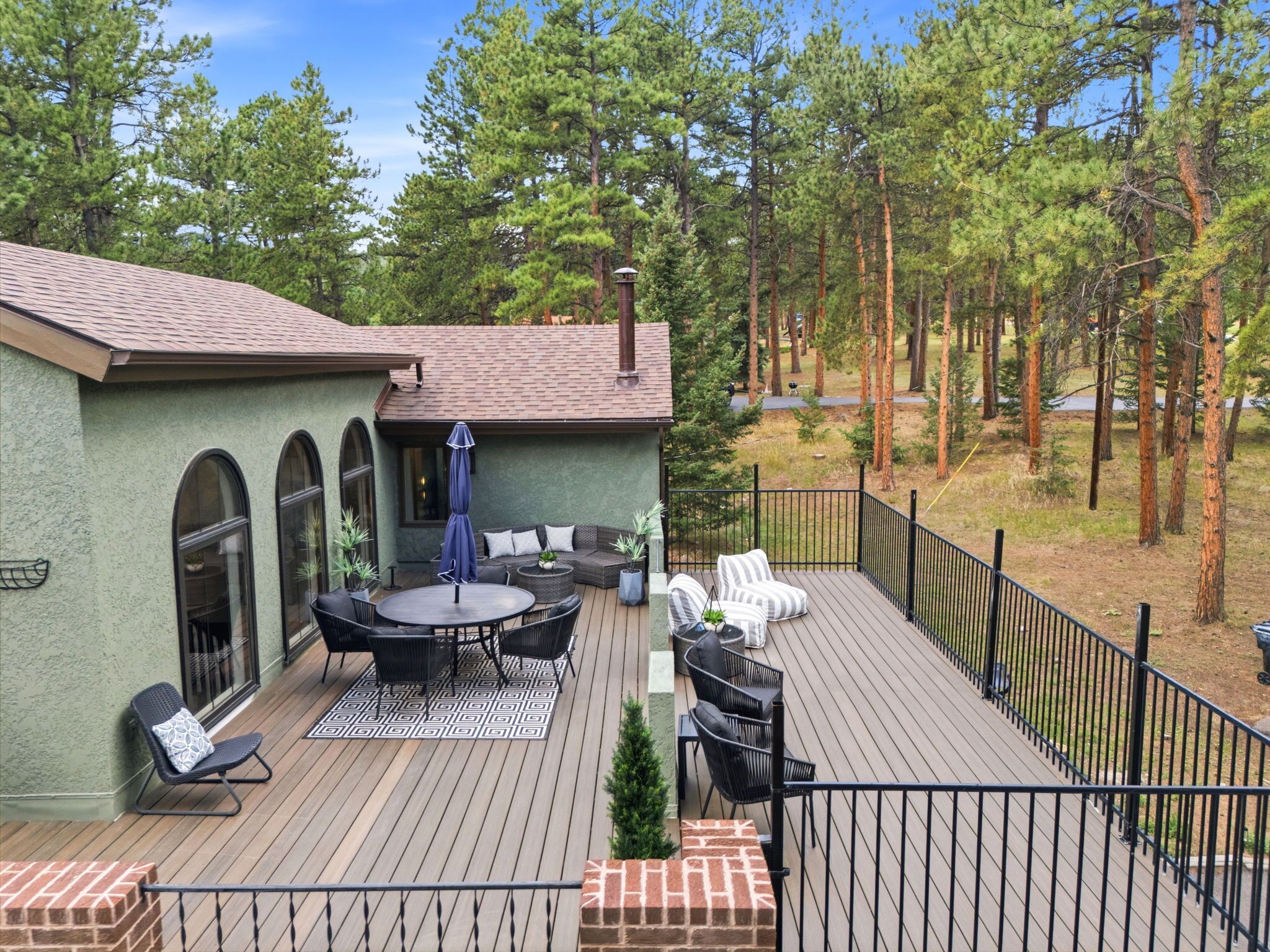 A deck with outdoor furniture, a covered seating area, and a view of a forested area.