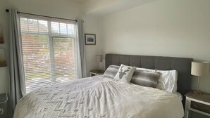 Une chambre avec un grand lit, un ventilateur de plafond, une fenêtre avec des stores et une table de chevet avec une lampe.