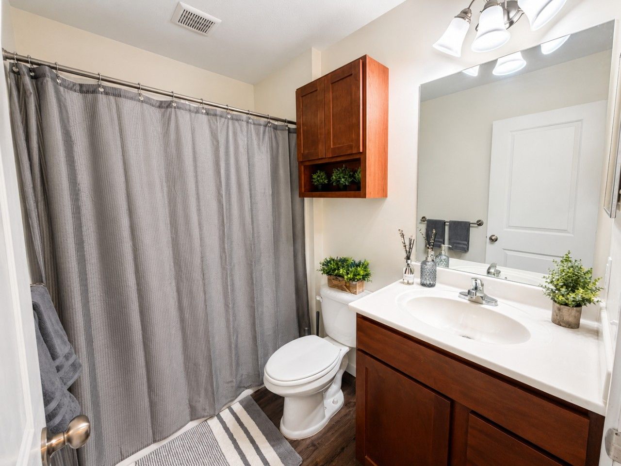 Une salle de bain avec un rideau de douche, des toilettes, un lavabo, un miroir et des meubles en bois.