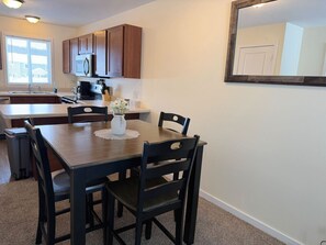 A dining area with a wooden table and chairs, a vase with flowers, and a kitchen in the background.