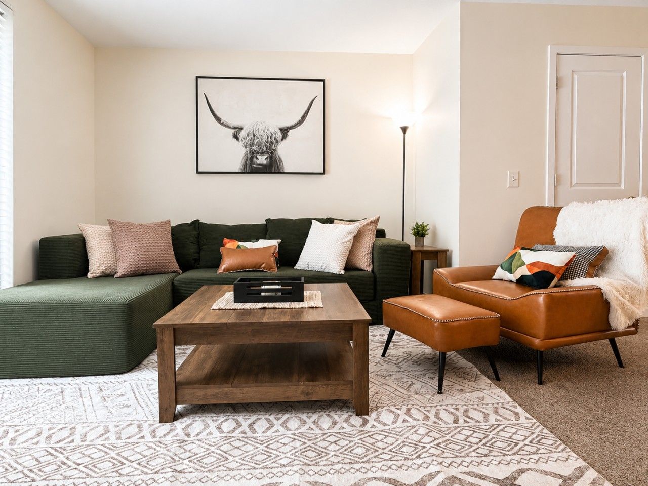 Un salon avec un canapé vert, une table basse en bois, un fauteuil en cuir marron et une œuvre d’art encadrée accrochée au mur.