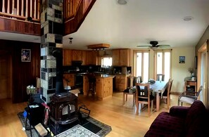 Een ruime woonkamer met een open haard, houten meubels, een eettafel en een keuken met houten kasten en een accentmuur van steen.