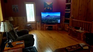 Olohuone, jossa on puulattia, televisio, lamppu ja sohva.