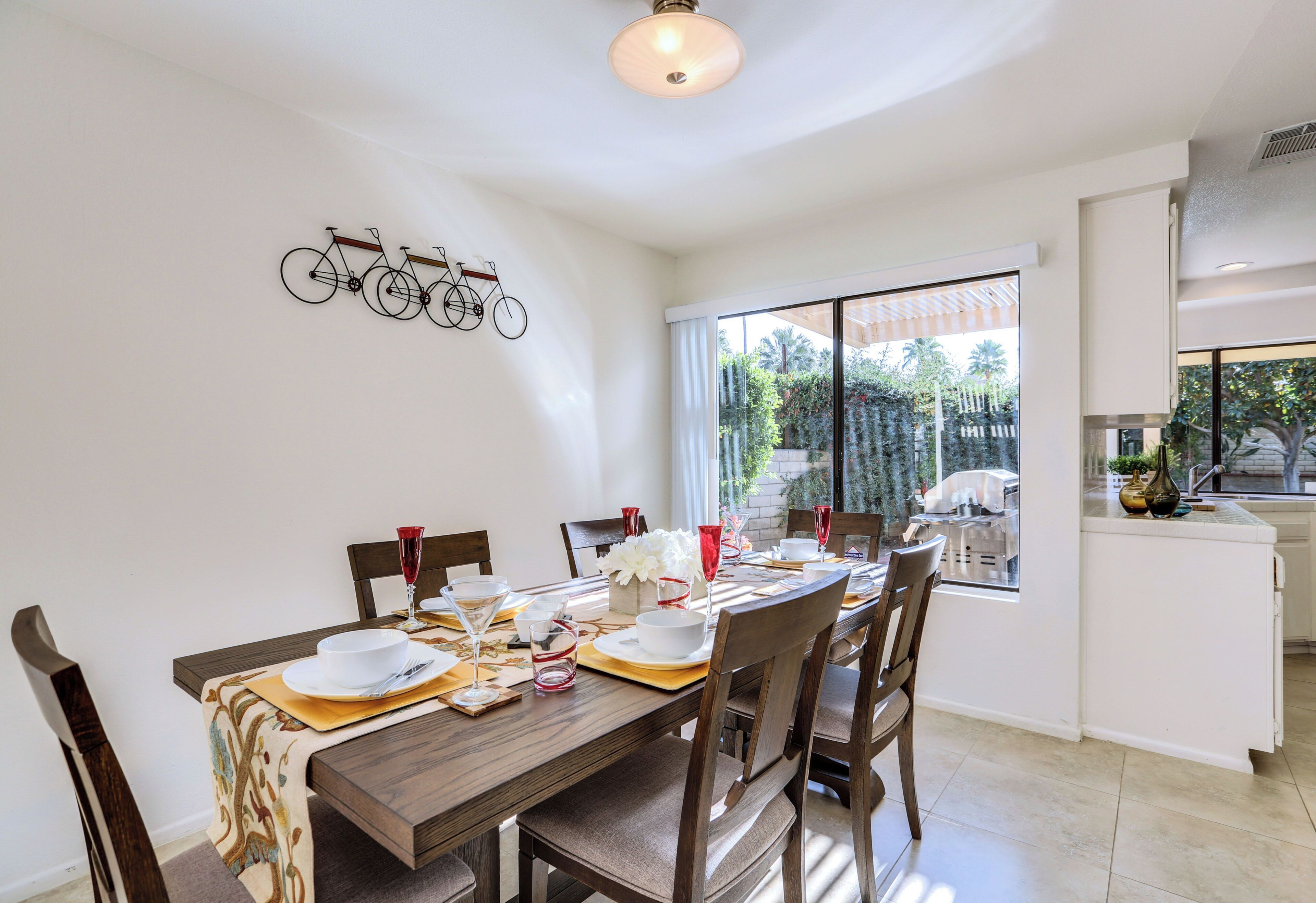 Un coin repas avec une table en bois dressée pour le repas, une œuvre d’art représentant un vélo accrochée au mur et une vue sur l’extérieur par une grande fenêtre.