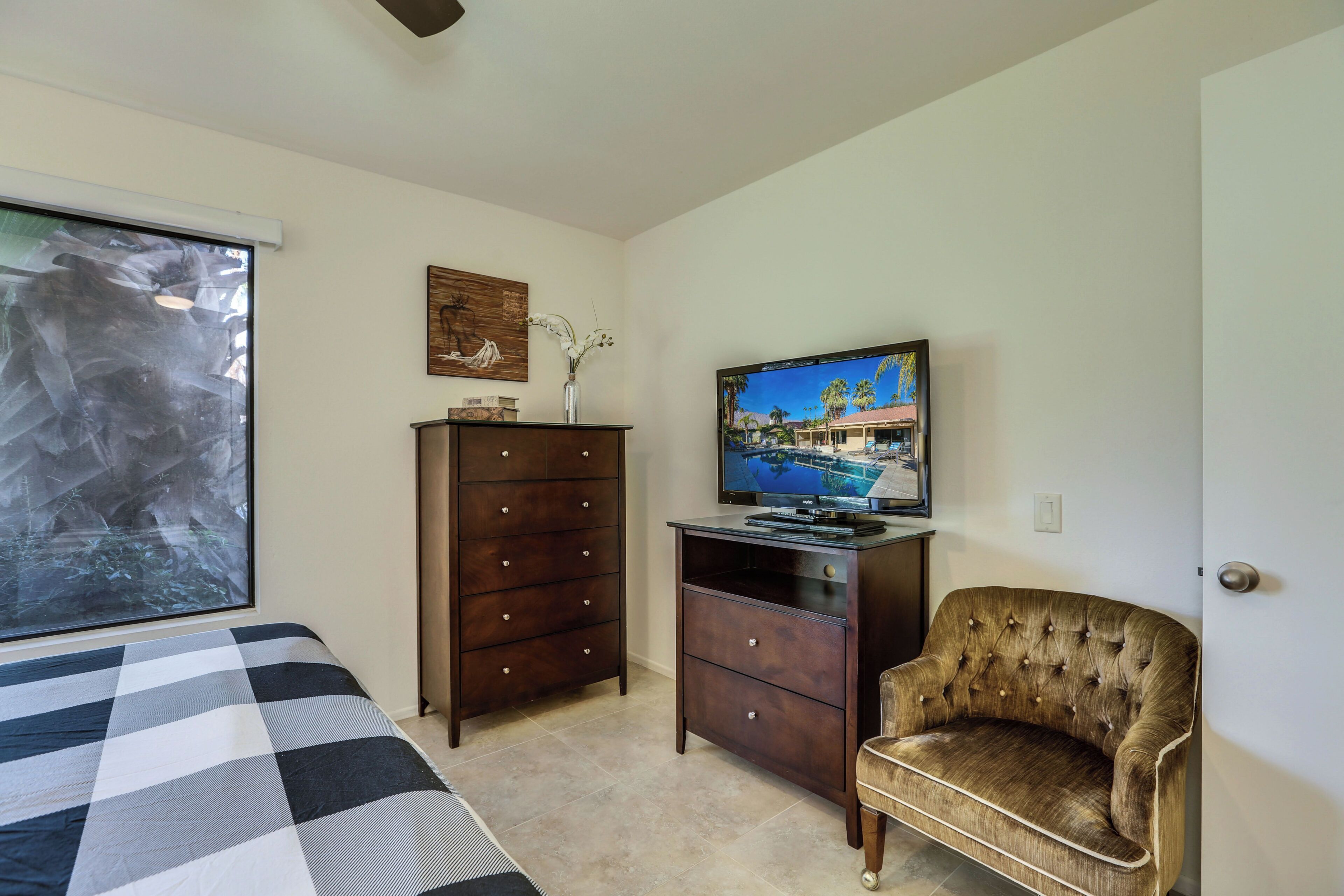 A bedroom with a bed, a dresser, a television, and a chair.