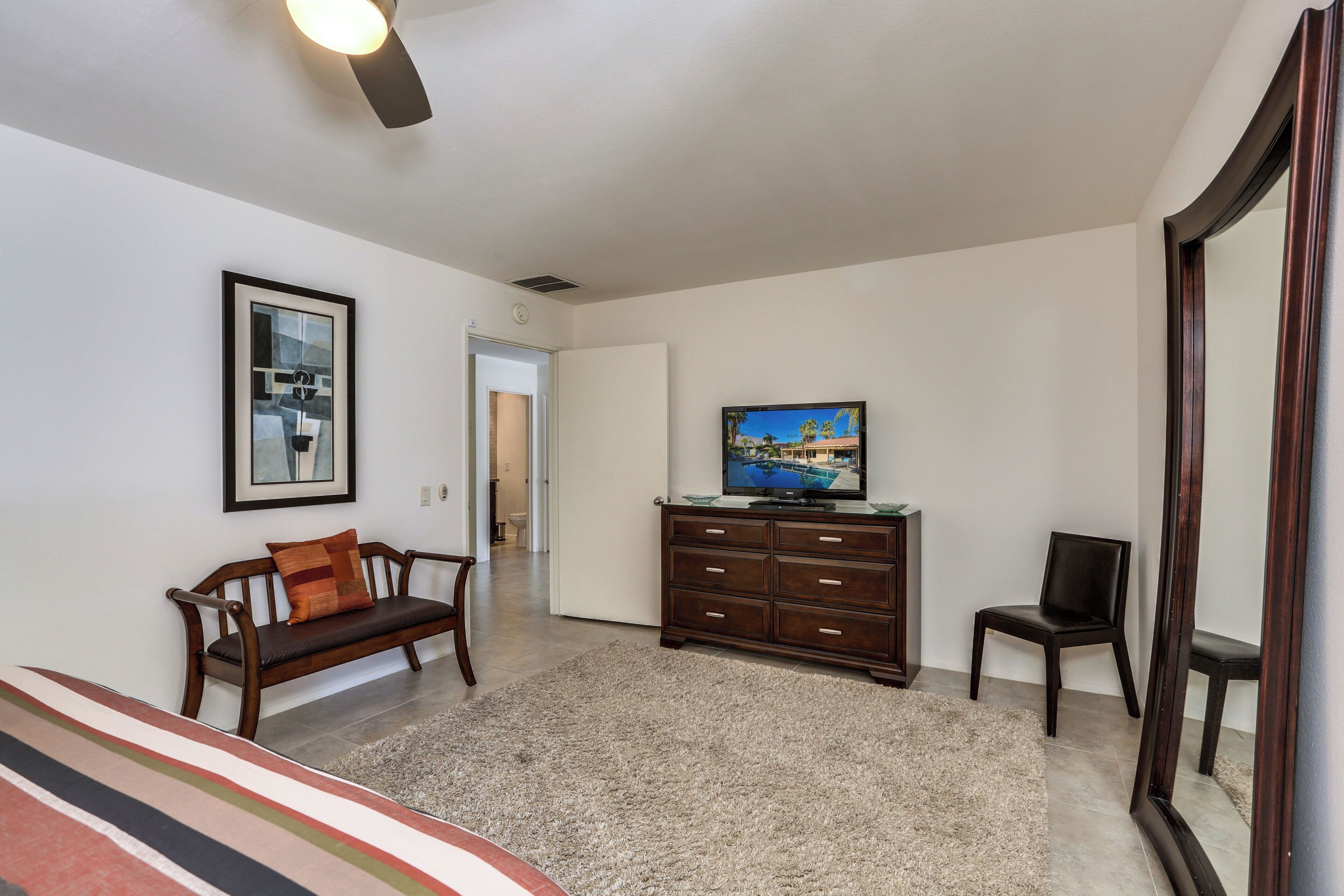 A room with a sofa, a television on a wooden cabinet, a chair, and a mirror.