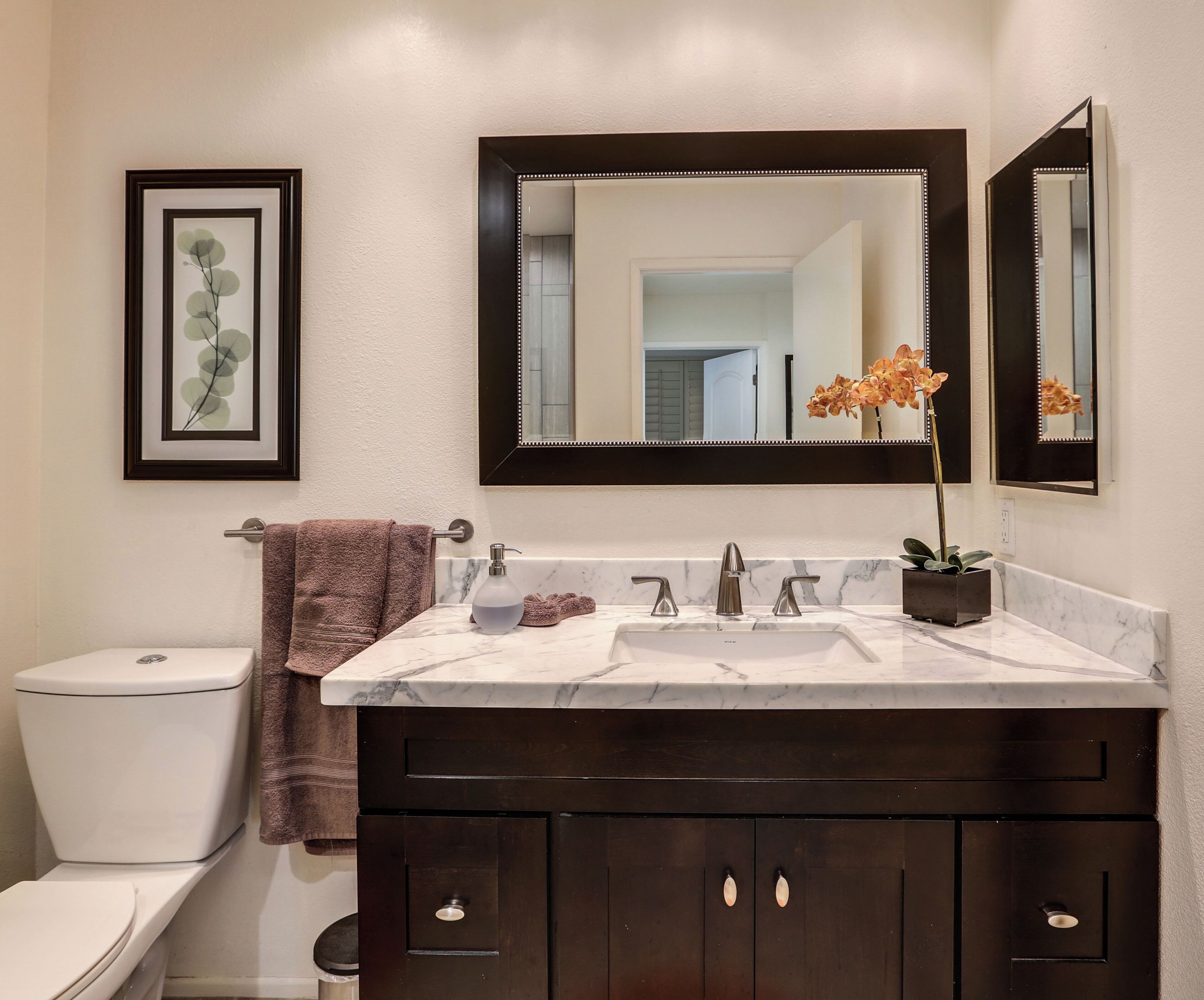 A bathroom with a white toilet, a dark wooden vanity with a mirror, and a marble sink.