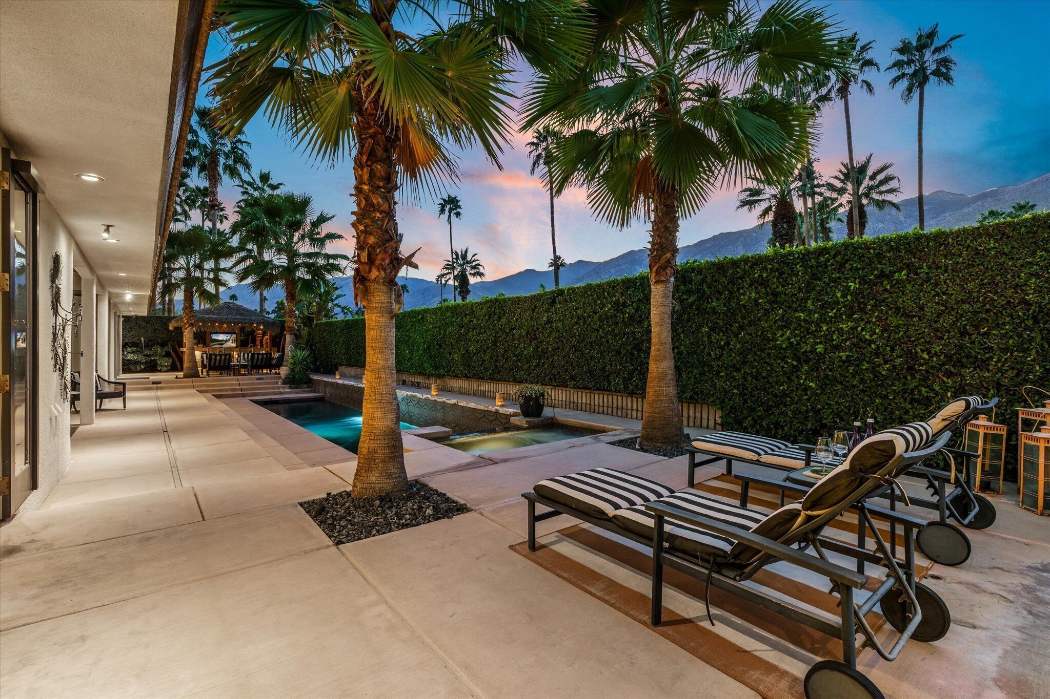 A pool area with lounge chairs, palm trees, and a view of mountains.