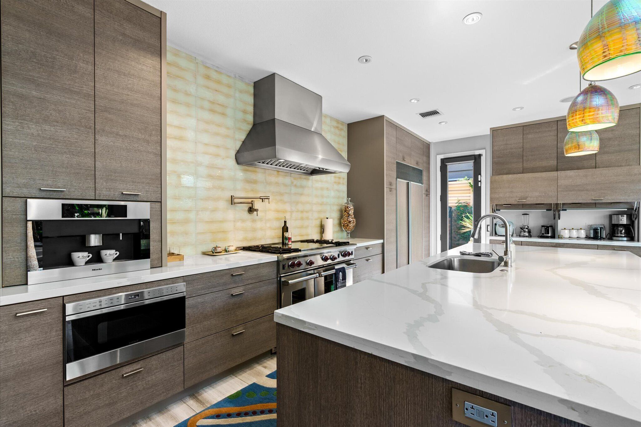 A modern kitchen with a large island, stainless steel appliances, and a unique backsplash.