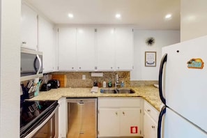 A compact kitchen with white cabinets, a microwave, a dishwasher, a refrigerator, and a granite countertop. - Biarritz B17 (Palm Springs)