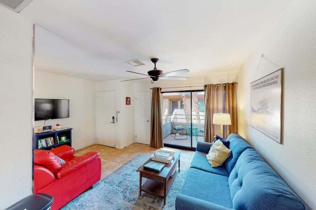 Un salon avec un canapé rouge, un canapé bleu, une table basse, un téléviseur et un ventilateur de plafond.