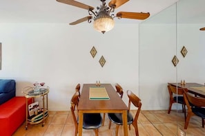 A dining area with a wooden table, chairs, a ceiling fan, and a small side table with a tray. - Biarritz B17 (Palm Springs)