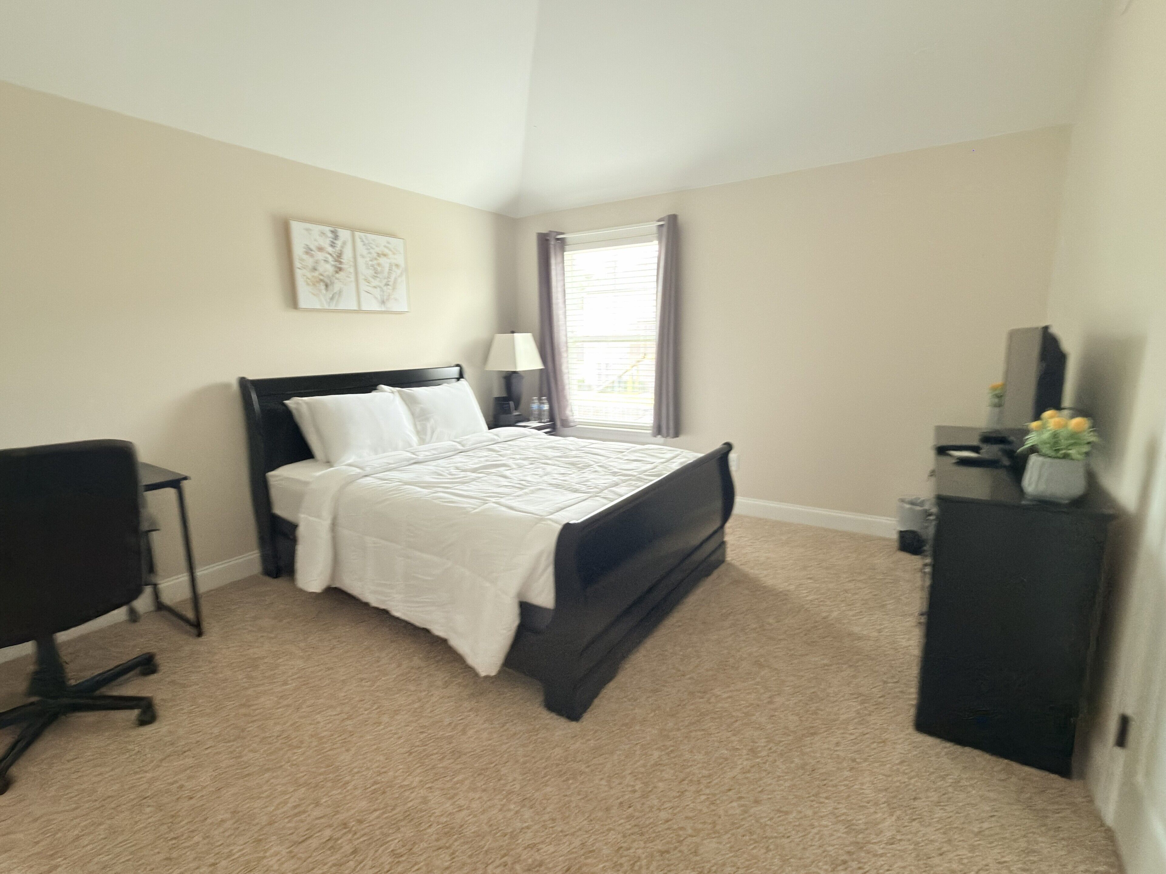 A bedroom with a bed, a desk, a chair, a dresser, and a window.