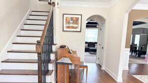 A staircase with wooden steps and black railings, a framed artwork on the wall, and a dining area in the background. - Elegant 5BR/4BA Masters Rental – Just 7 Miles from Augusta National (Martinez)