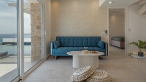 Una sala de estar moderna con un sofá azul, una mesa de centro redonda y vista al mar a través de amplios ventanales.