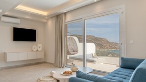 Una sala de estar moderna con un sofá, una mesita baja con un cuenco de bocadillos, un televisor montado en la pared y un amplio ventanal corredera que da a un balcón con vistas al paisaje.