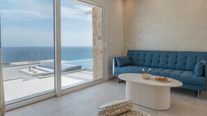 Una sala de estar moderna con un sofá azul, una mesa redonda de centro y un gran ventanal corredizo que da a un balcón con vista al mar.