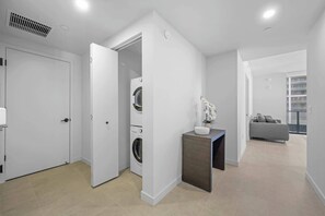 A modern apartment with a laundry room, a small side table with a vase, and a grey sofa in the living area. - 2408 New Luxury Downtown Retreat, Gym, & Prime Location 1B1B (Miami)