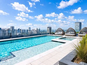 Ein Pool auf dem Dach mit klarem, blauem Wasser, umgeben von Liegestühlen und Blick auf die Stadt.
